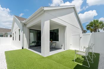 The exterior of a white house with a lawn and two chairs
